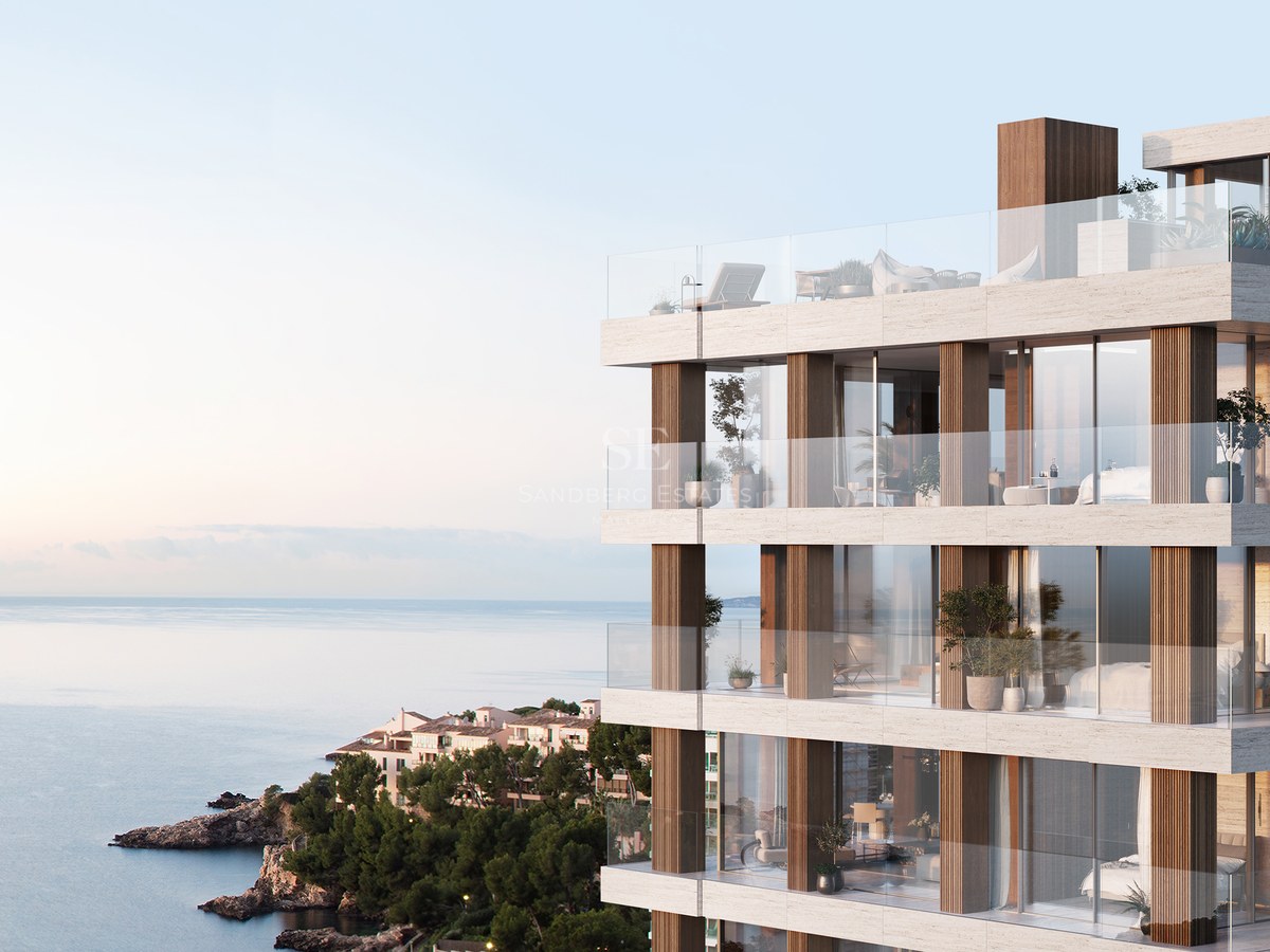 Modern multi-story building with stone facade, glass balconies, and panoramic sea views at sunset.