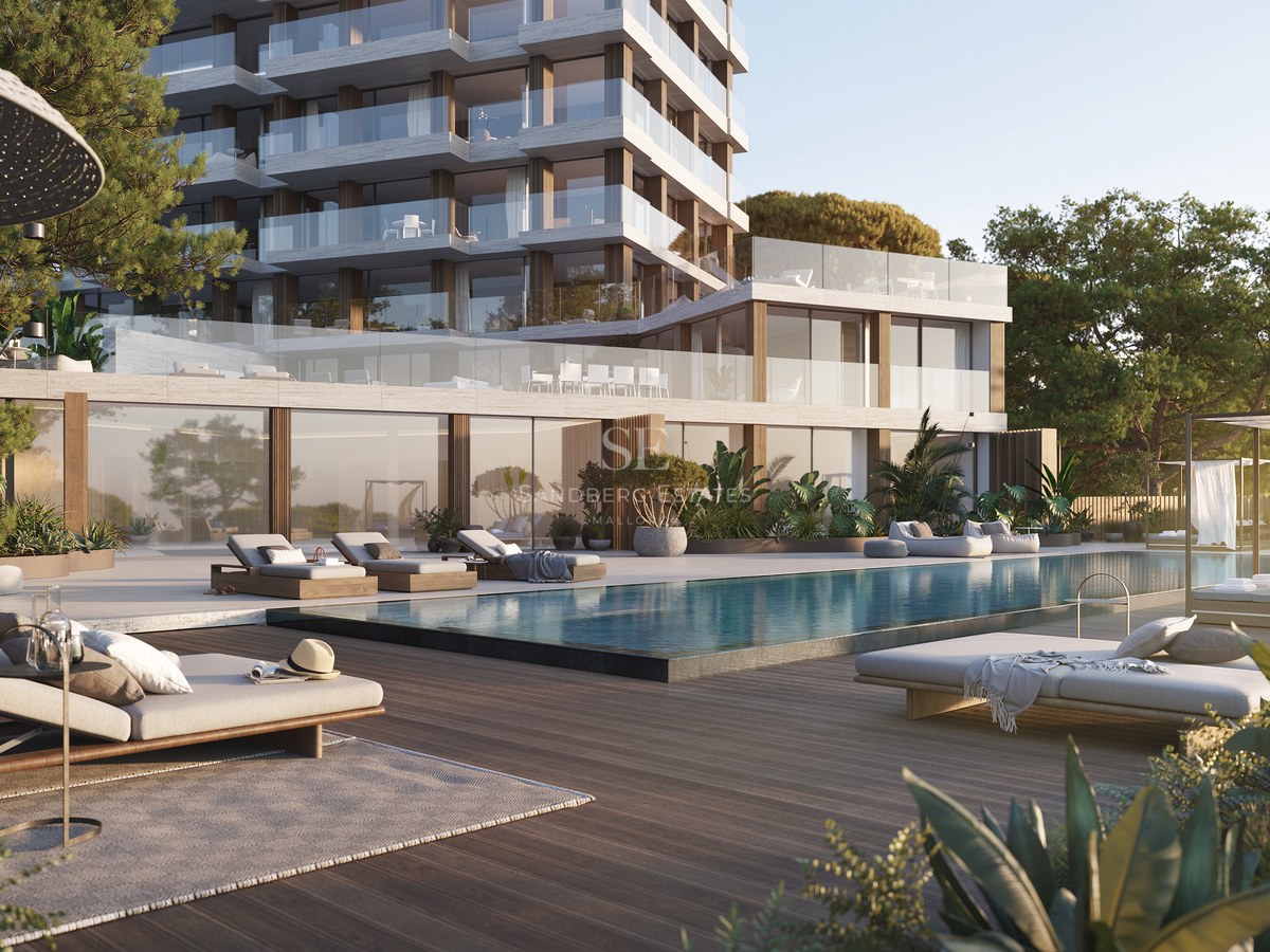 Modern apartment building with a large swimming pool, wooden deck, luxury lounge chairs, and lush green gardens.