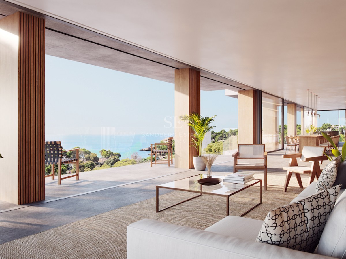 Modern open-plan living room with floor-to-ceiling windows opening to a terrace overlooking the ocean and coast.