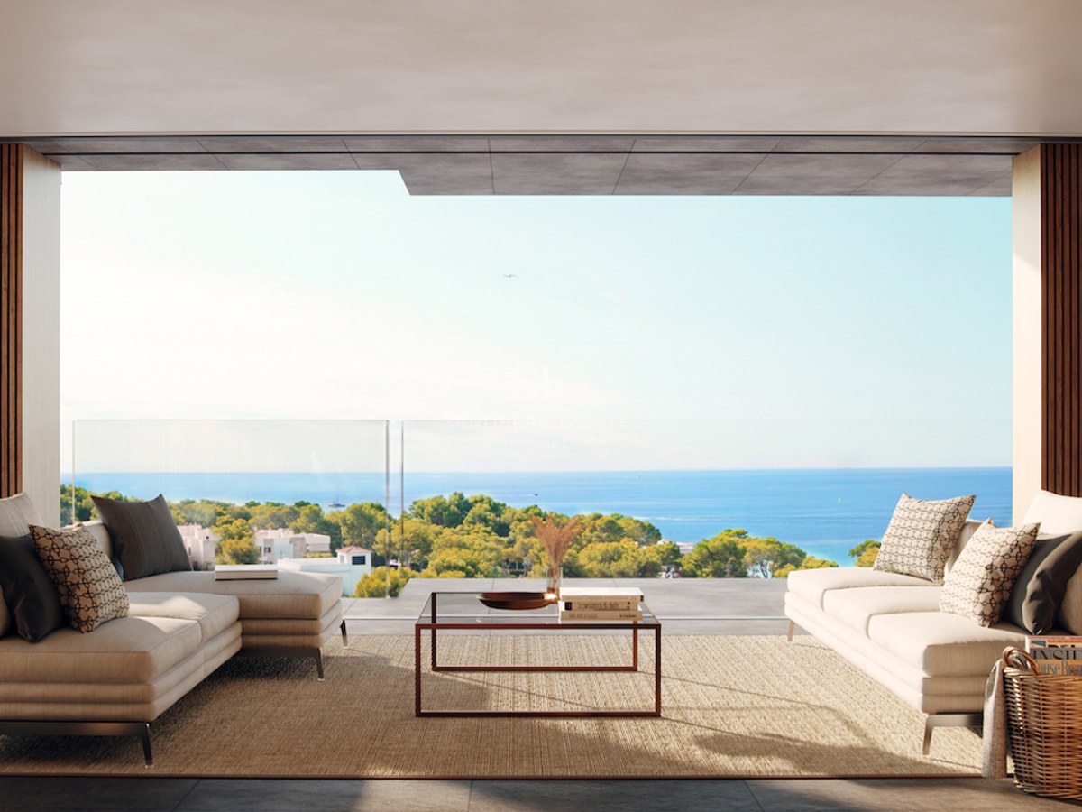 Modern terrace with beige sofas and glass railing overlooking the Mediterranean Sea and lush greenery.