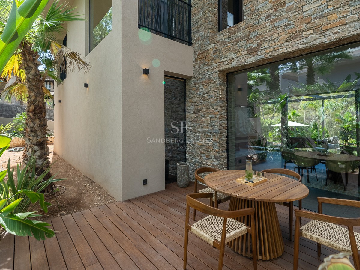 Contemporary wooden terrace featuring a round dining set, natural stone wall, and tropical garden backdrop.