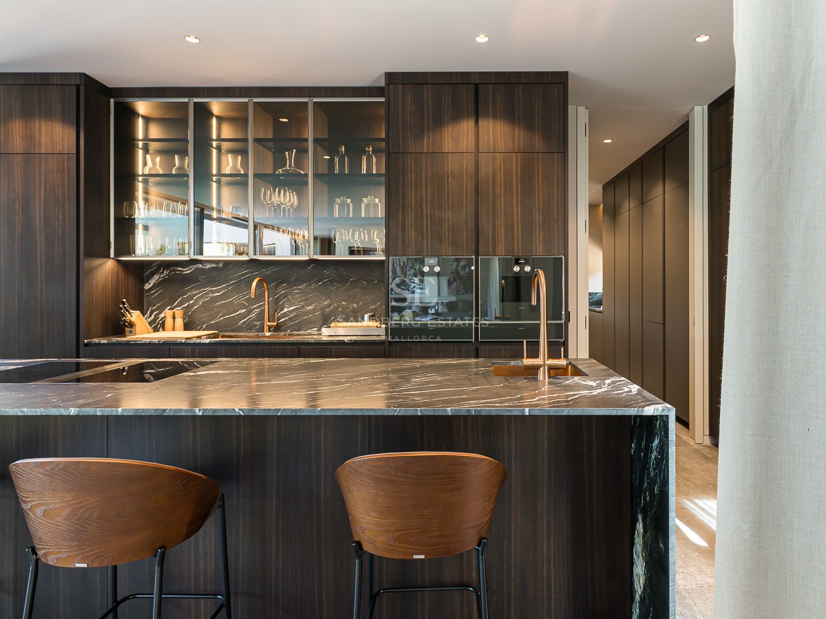 Contemporary kitchen featuring a dark veined marble island, wooden bar stools, and elegant copper fixtures.