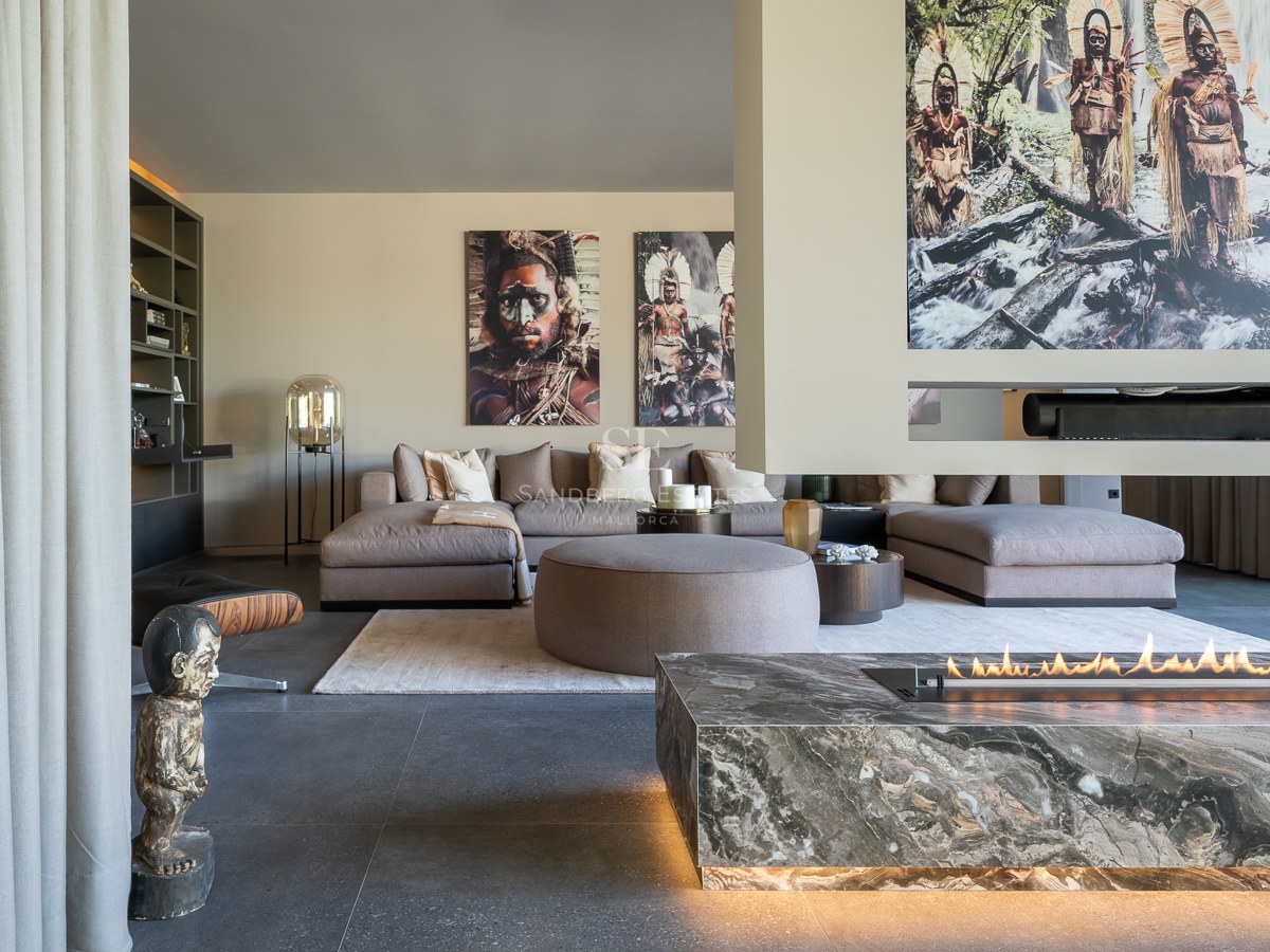 Luxury living room featuring a grey sectional sofa, a linear marble fireplace, and tribal artwork on the walls.