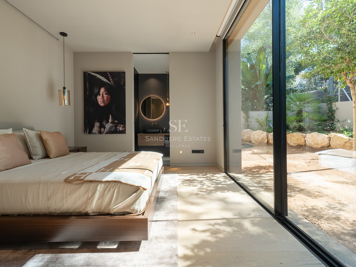 Modern bedroom featuring floor-to-ceiling glass doors to a garden, walnut wood bed frame, and ensuite bathroom.
