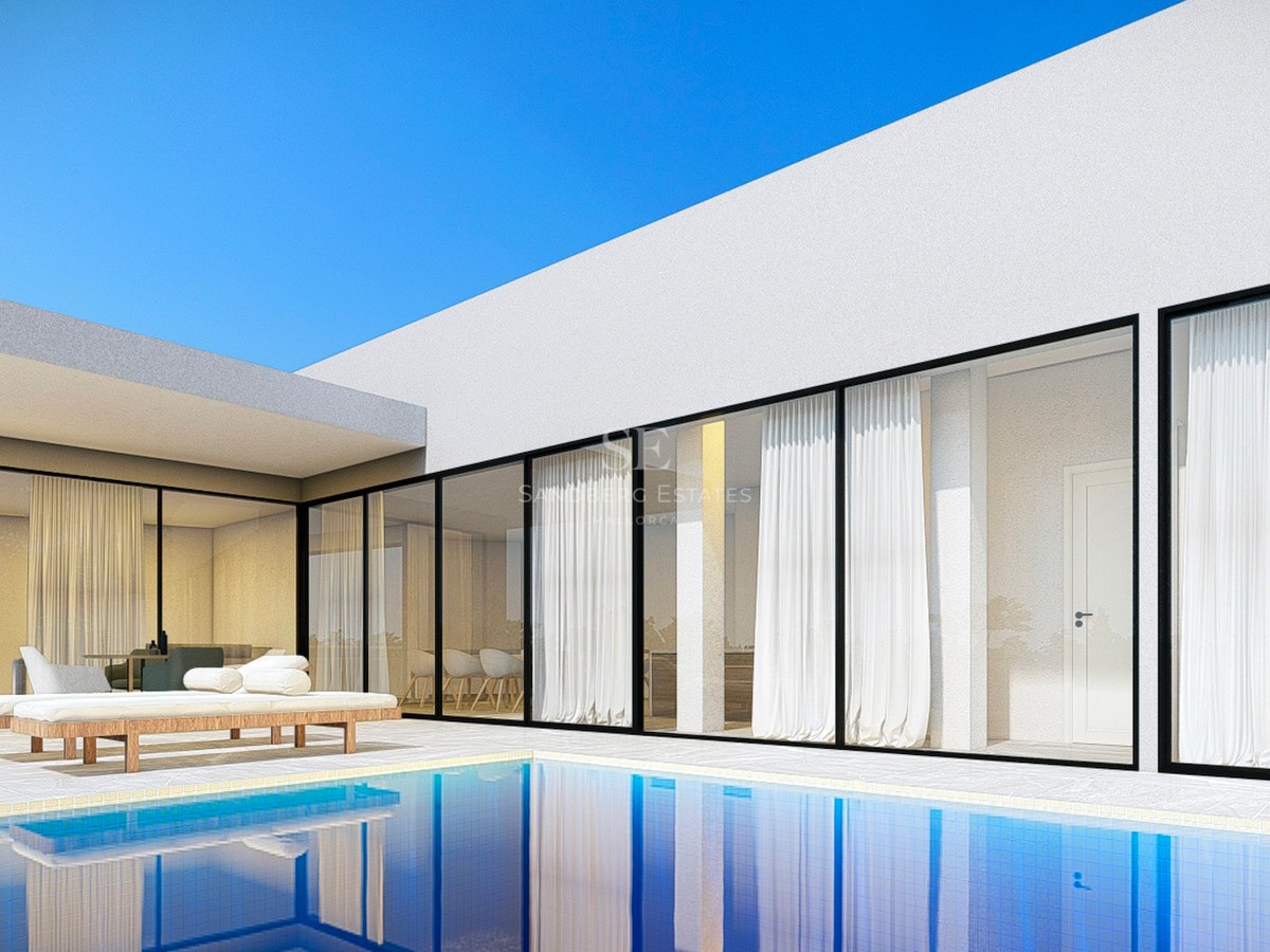 Modern white villa with floor-to-ceiling glass windows overlooking a blue swimming pool and stone terrace with sun loungers.