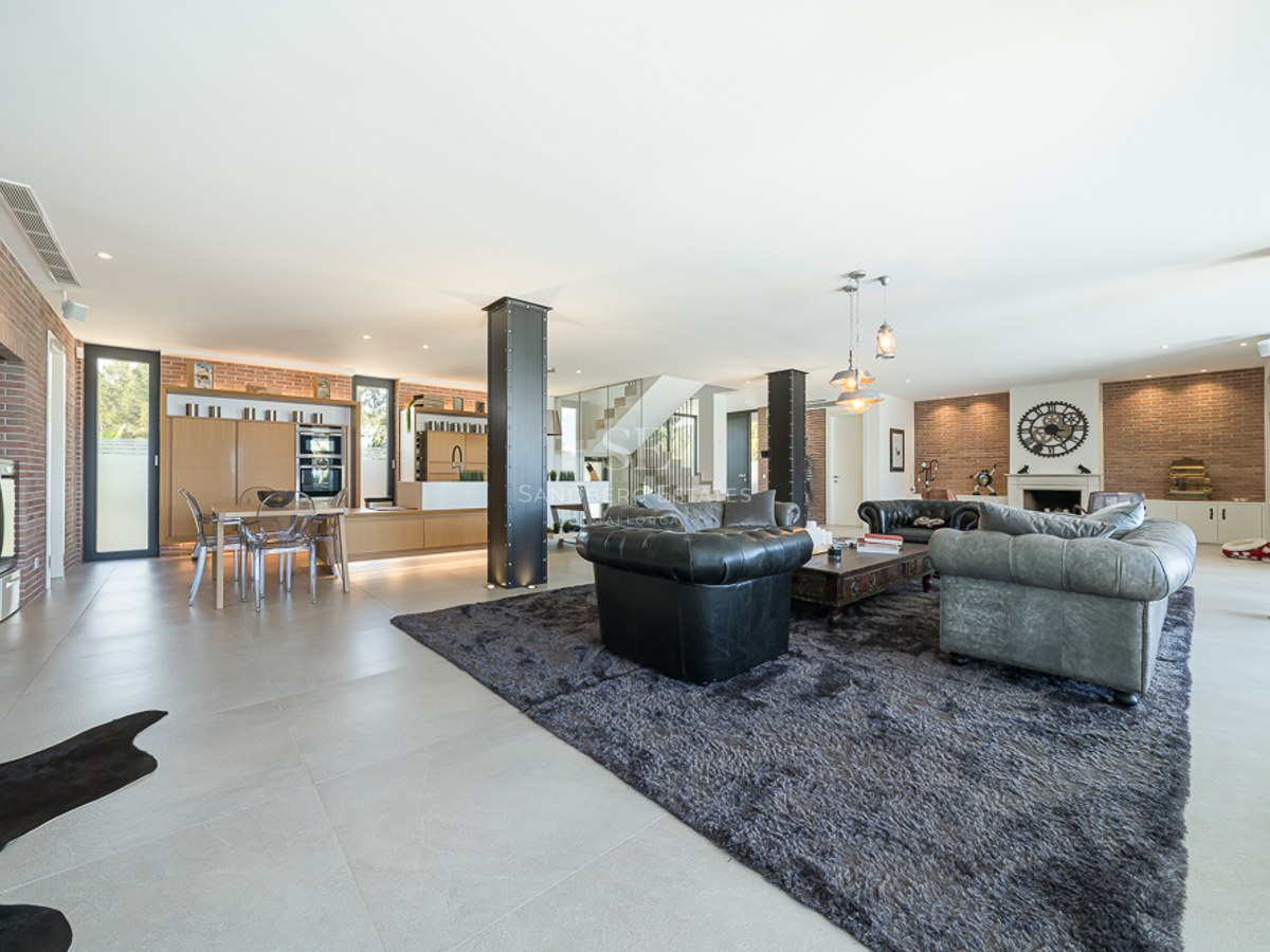 Vaste salon avec baies vitrées, piscine reflétant la lumière, design moderne, canapés en cuir et table basse élégante. Éclairage naturel.