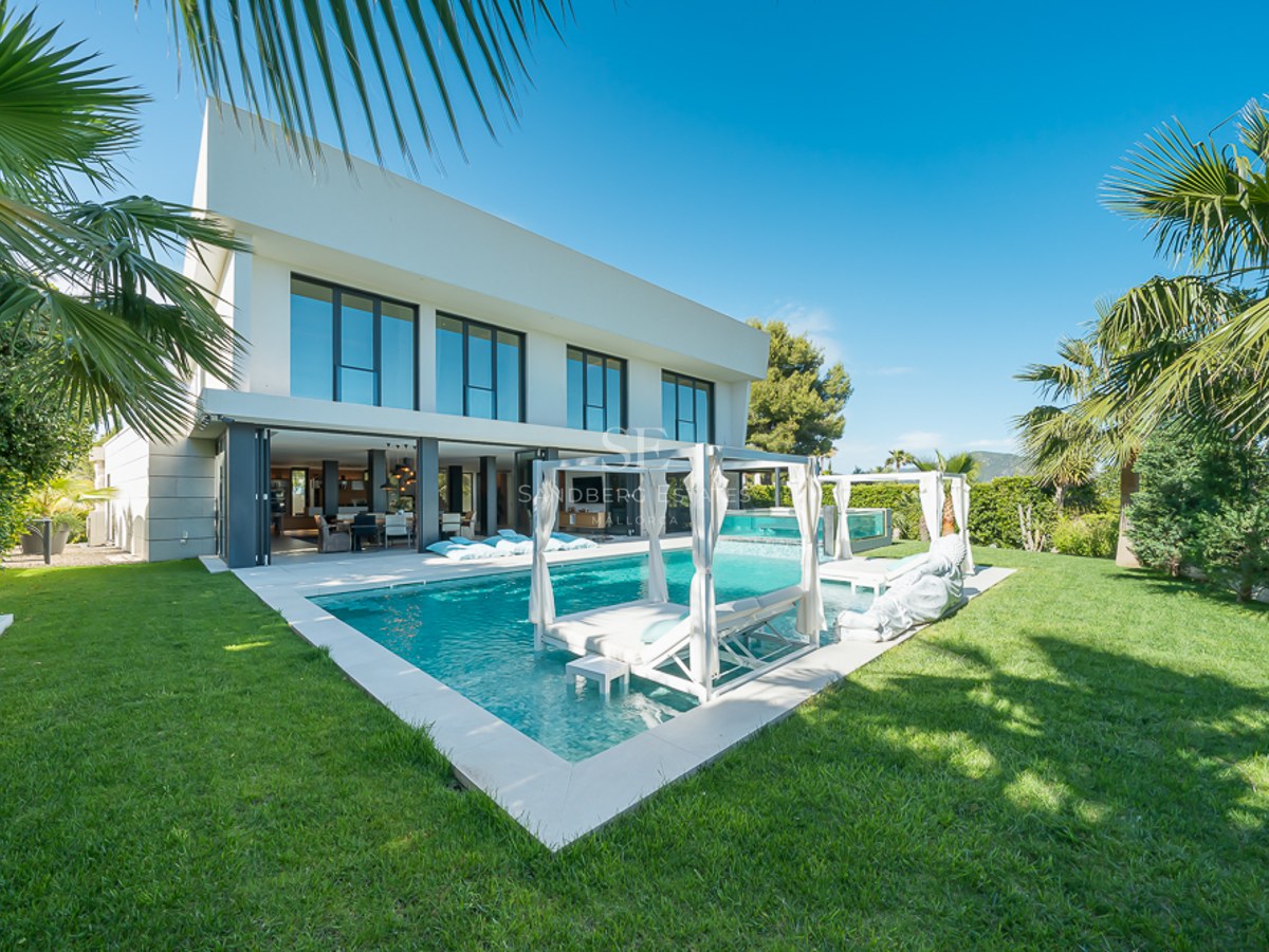 Vue de la piscine turquoise entourée d'une végétation luxuriante et d'une architecture moderne. Chaises longues et parasols blancs invitent à la détente.