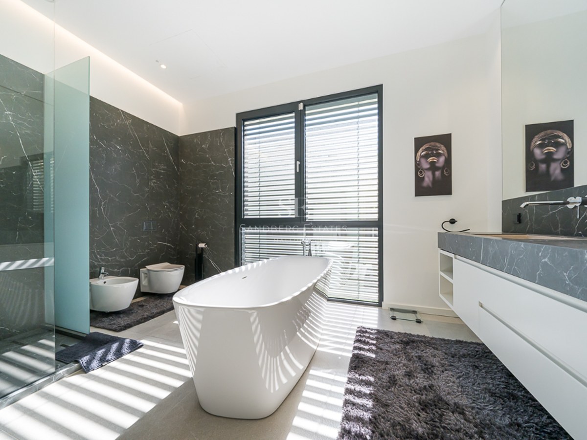 Vue de la villa avec piscine à débordement, chaises longues et végétation luxuriante. Design moderne avec de grandes fenêtres et des couleurs claires.