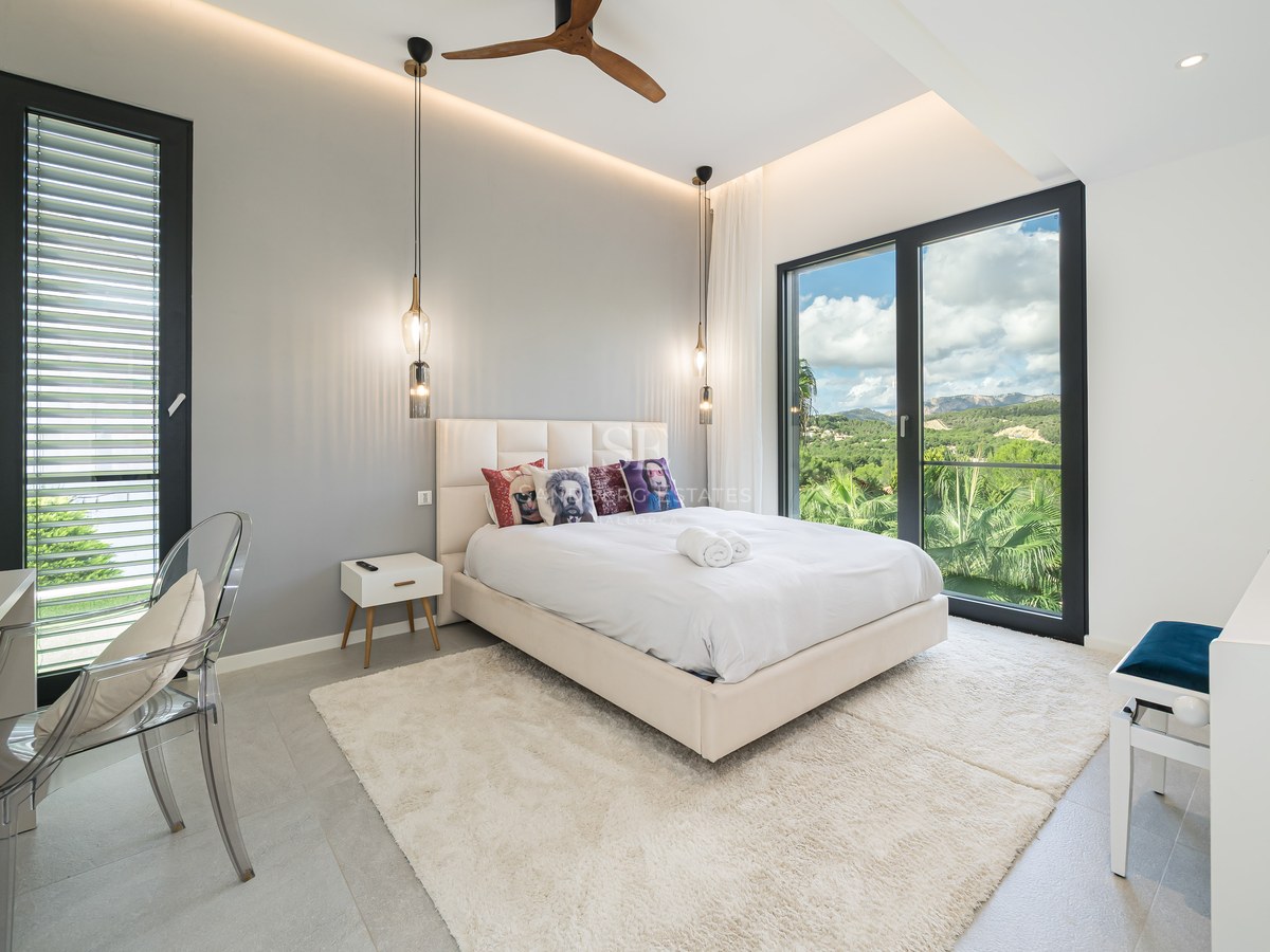 Chambre moderne avec grand lit, baies vitrées donnant sur les montagnes, chaise transparente et éclairage design.