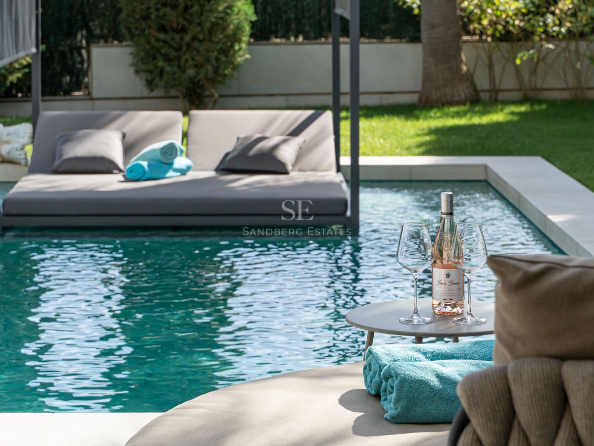 Piscine de luxe avec un lit de repos flottant gris, une table avec du vin rosé et des serviettes turquoise.