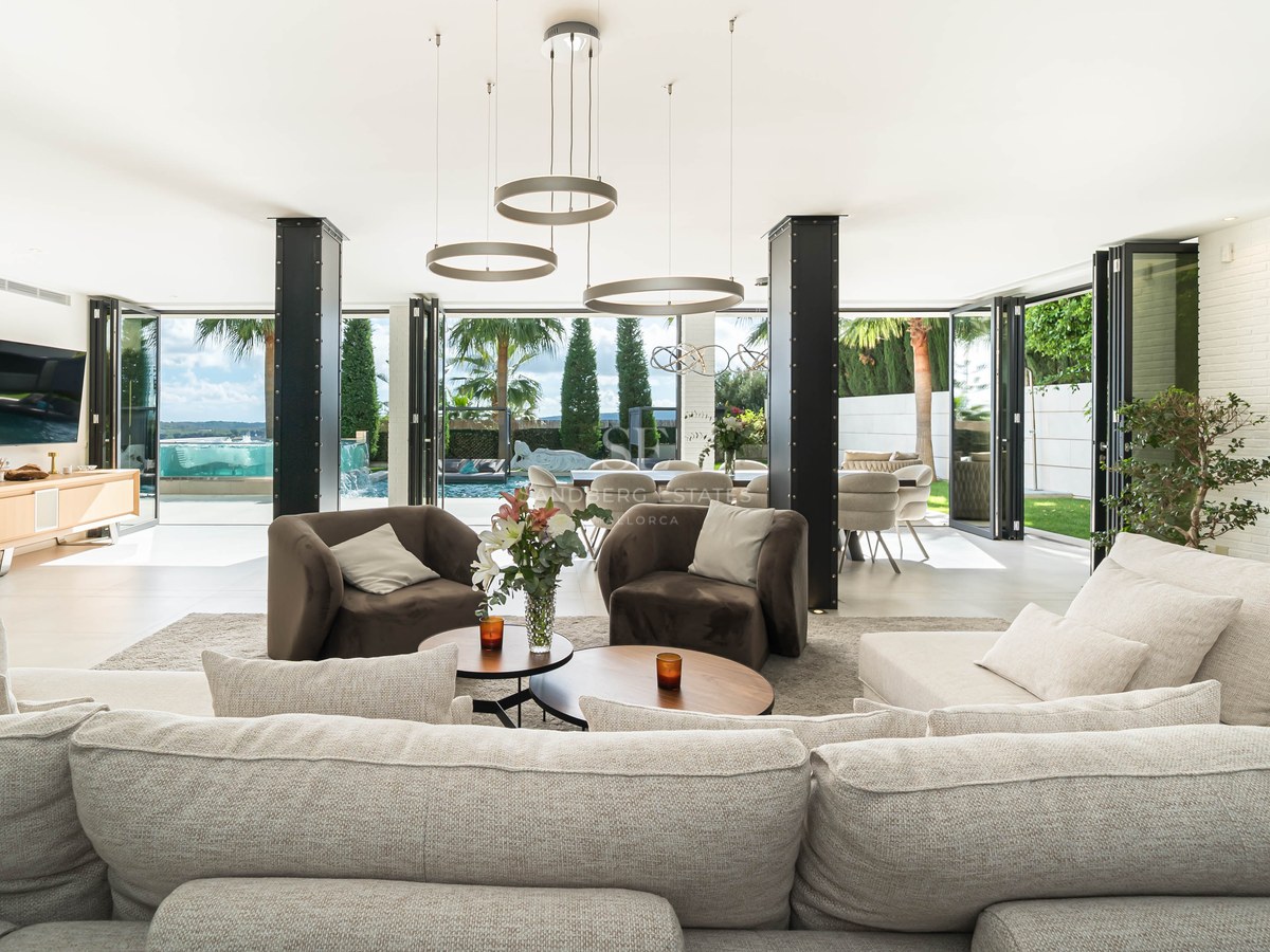 Salon moderne avec canapé d'angle crème, piliers en acier et baies vitrées accordéon ouvrant sur la piscine.
