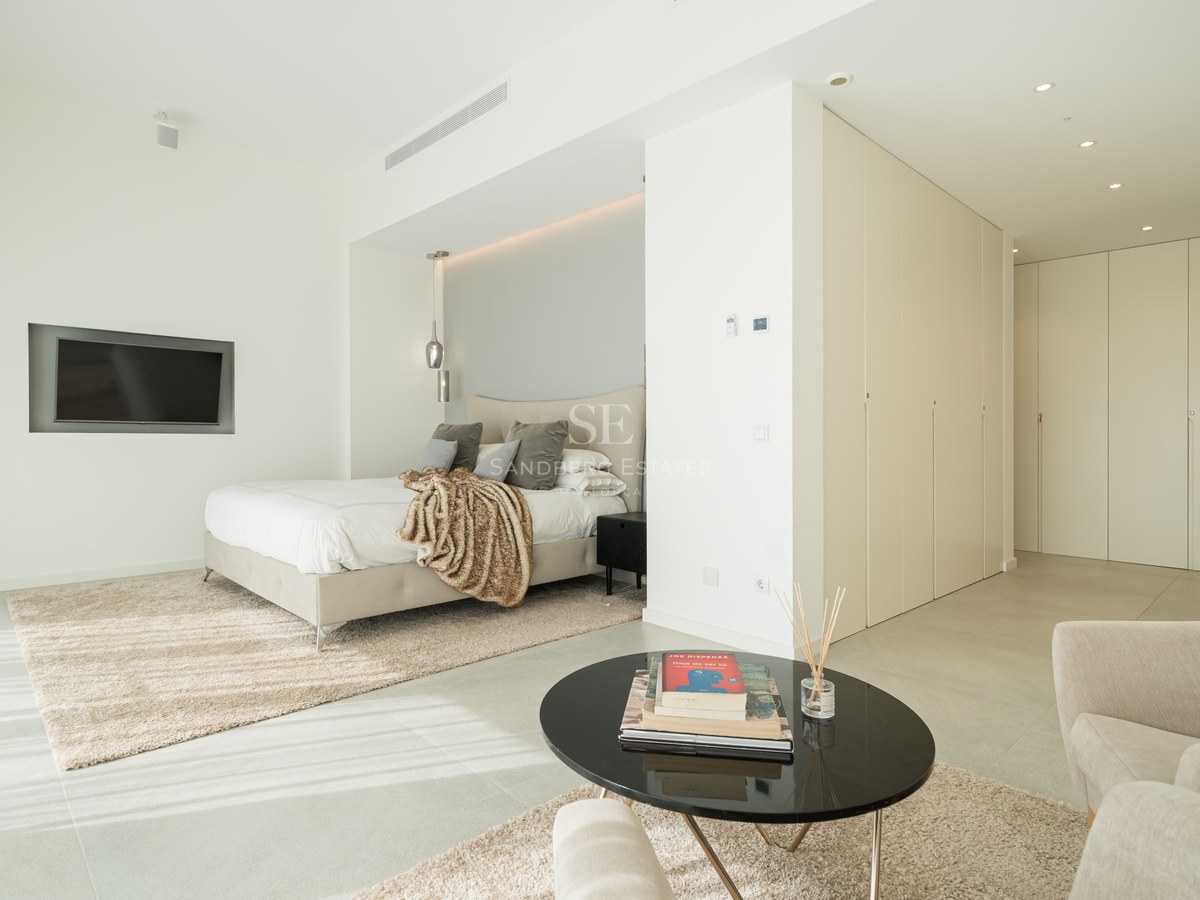 Chambre principale moderne avec lit design, placards intégrés, coin salon et sol en grès grand format.