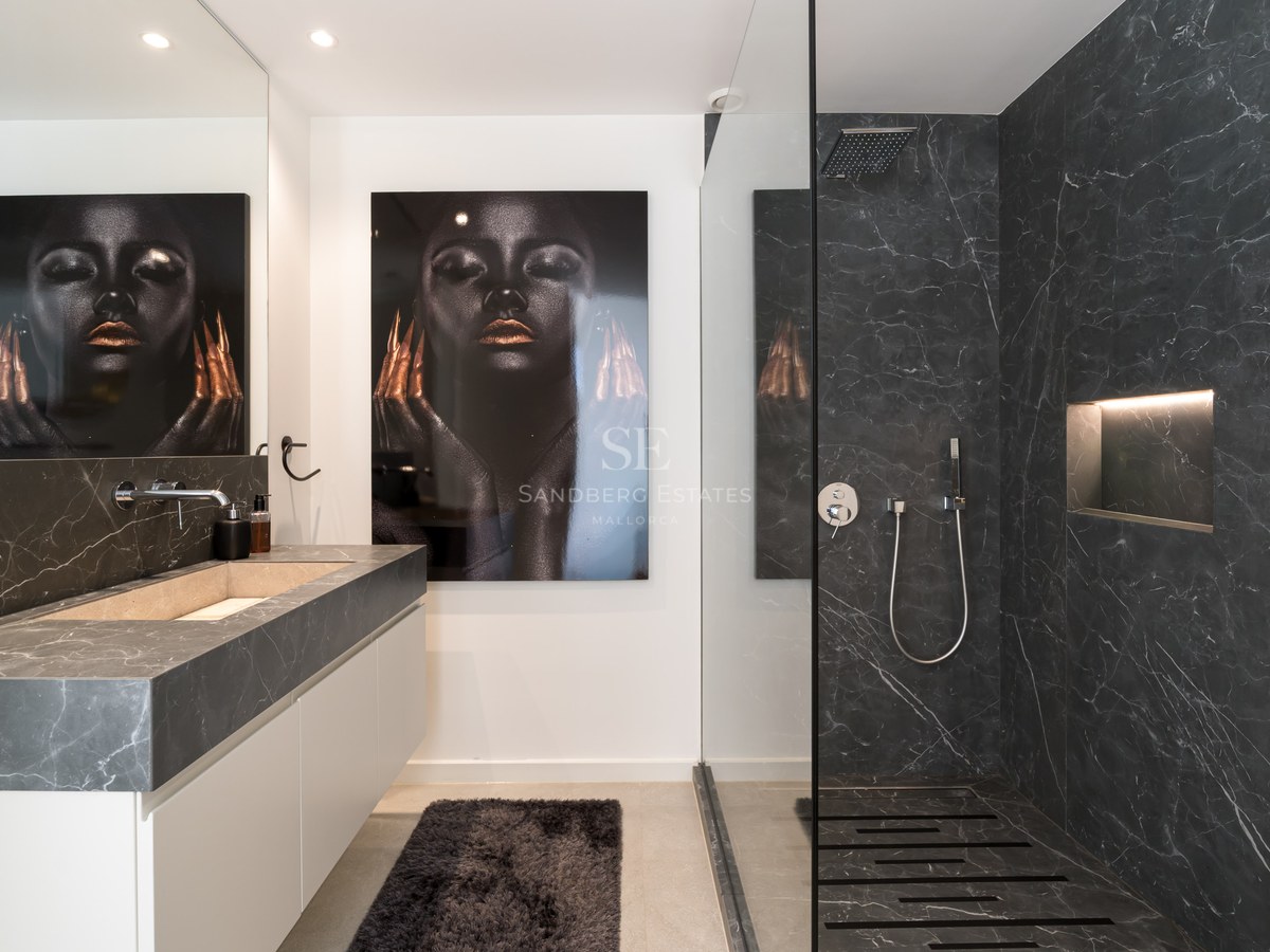 Salle de bain contemporaine avec murs en marbre sombre, douche en verre et vasque intégrée en pierre.