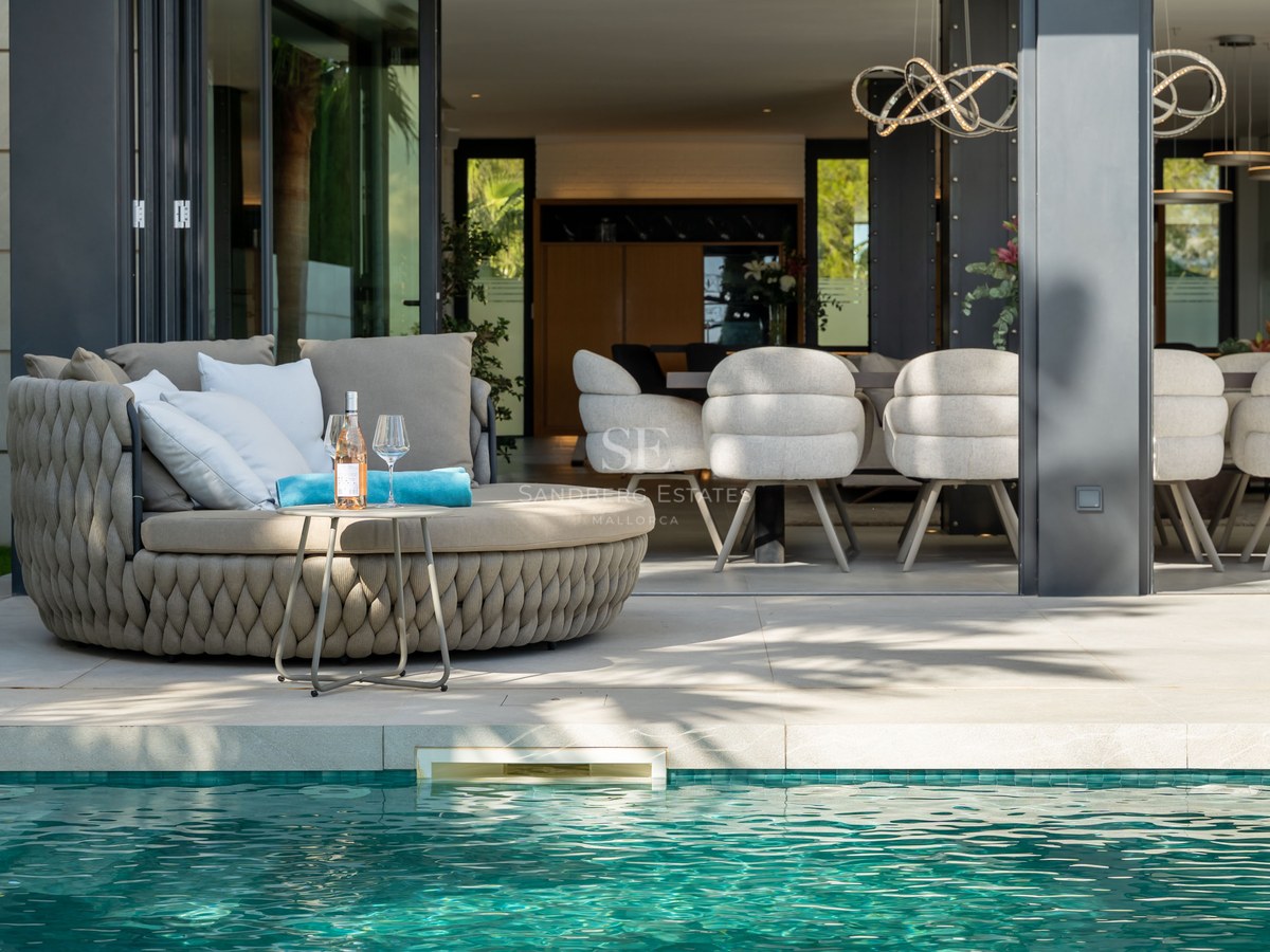 Terrasse de luxe avec bain de soleil tressé au bord d'une piscine turquoise, vue sur l'intérieur moderne.