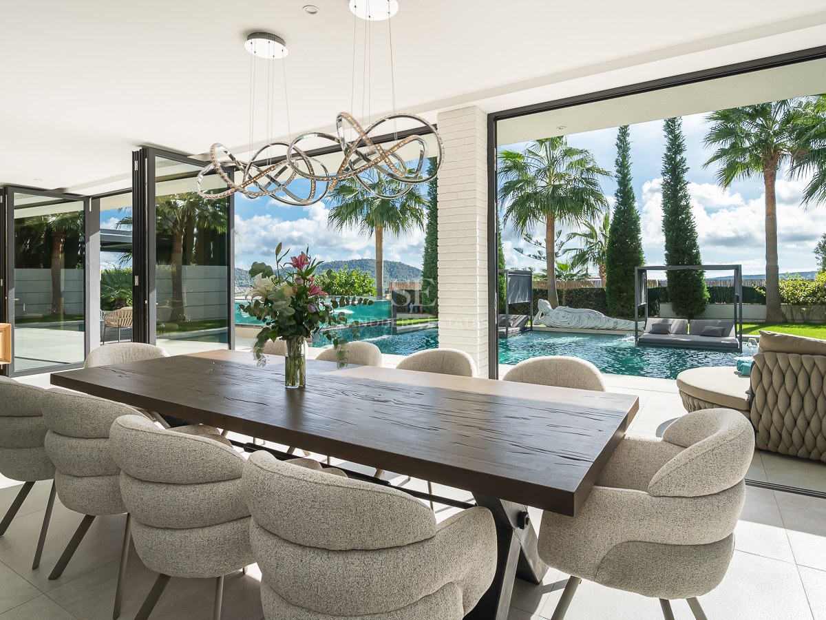 Salle à manger moderne avec table en bois et chaises élégantes s'ouvrant sur une piscine privée et des palmiers.