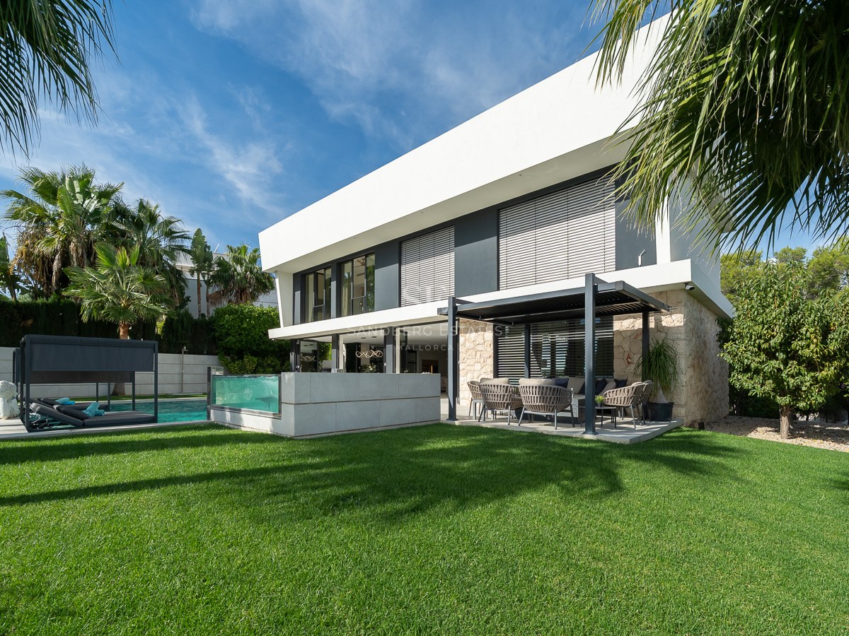 Villa moderne de deux étages avec pierre, piscine à paroi de verre et terrasse couverte sur une pelouse verdoyante.