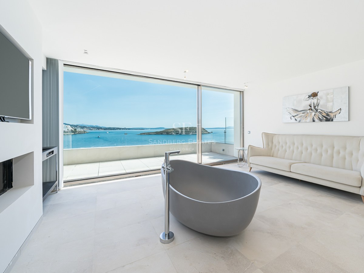 Baño moderno con bañera gris exenta, sofá crema y grandes ventanales con vistas panorámicas al mar.