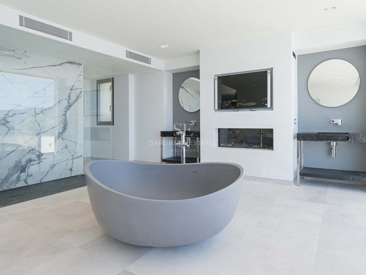 Baño moderno con bañera gris, ducha con pared de mármol y lavabos dobles con espejos redondos.