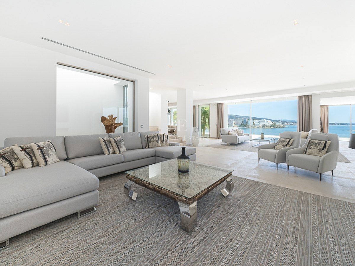 Amplio salón moderno con sofás gris claro, mesa de centro de cristal y grandes ventanales con vistas al mar Mediterráneo.
