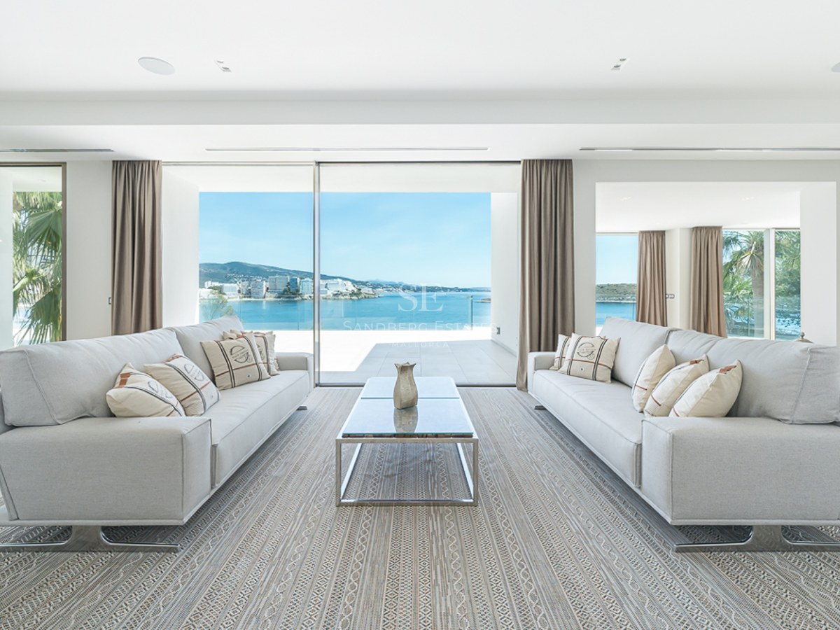 Salón luminoso con dos sofás grises, mesa de centro de cristal y grandes ventanales con vistas al mar.