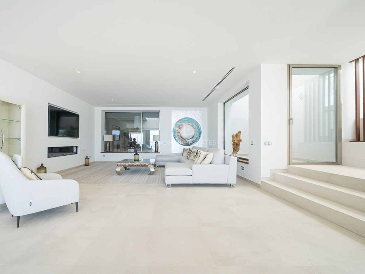 Salón minimalista luminoso con sofá blanco, suelos de piedra, chimenea lineal y arte moderno.