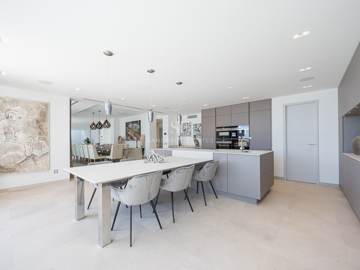 Cocina moderna con armarios grises, isla blanca con mesa de comedor y sillas de terciopelo gris.