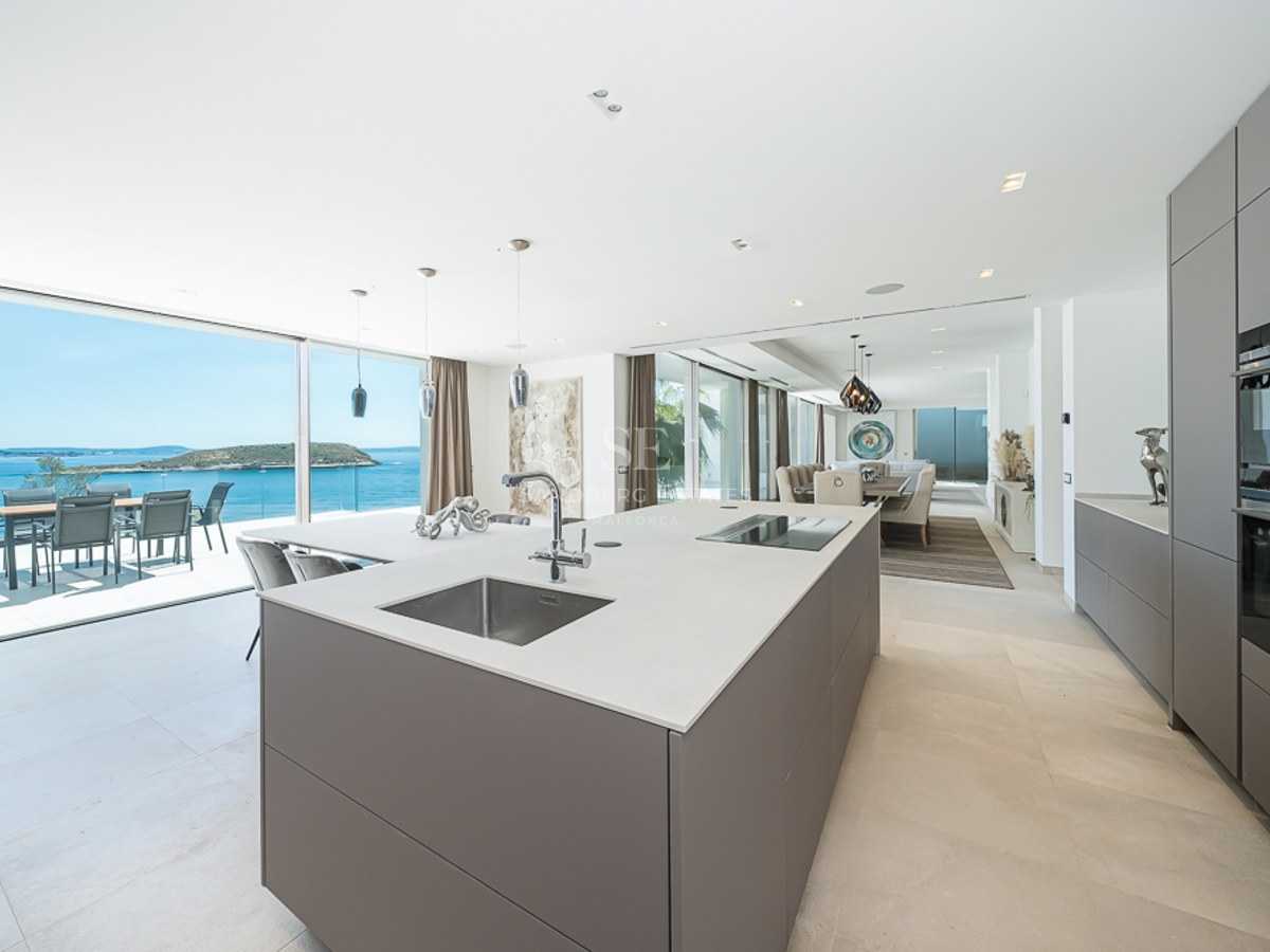 Isla de cocina minimalista frente a una terraza con vistas al océano y una isla a lo lejos.
