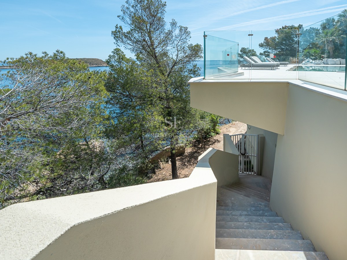 Terraza de lujo con barandillas de cristal y escaleras de piedra con vistas al mar Mediterráneo y pinos.