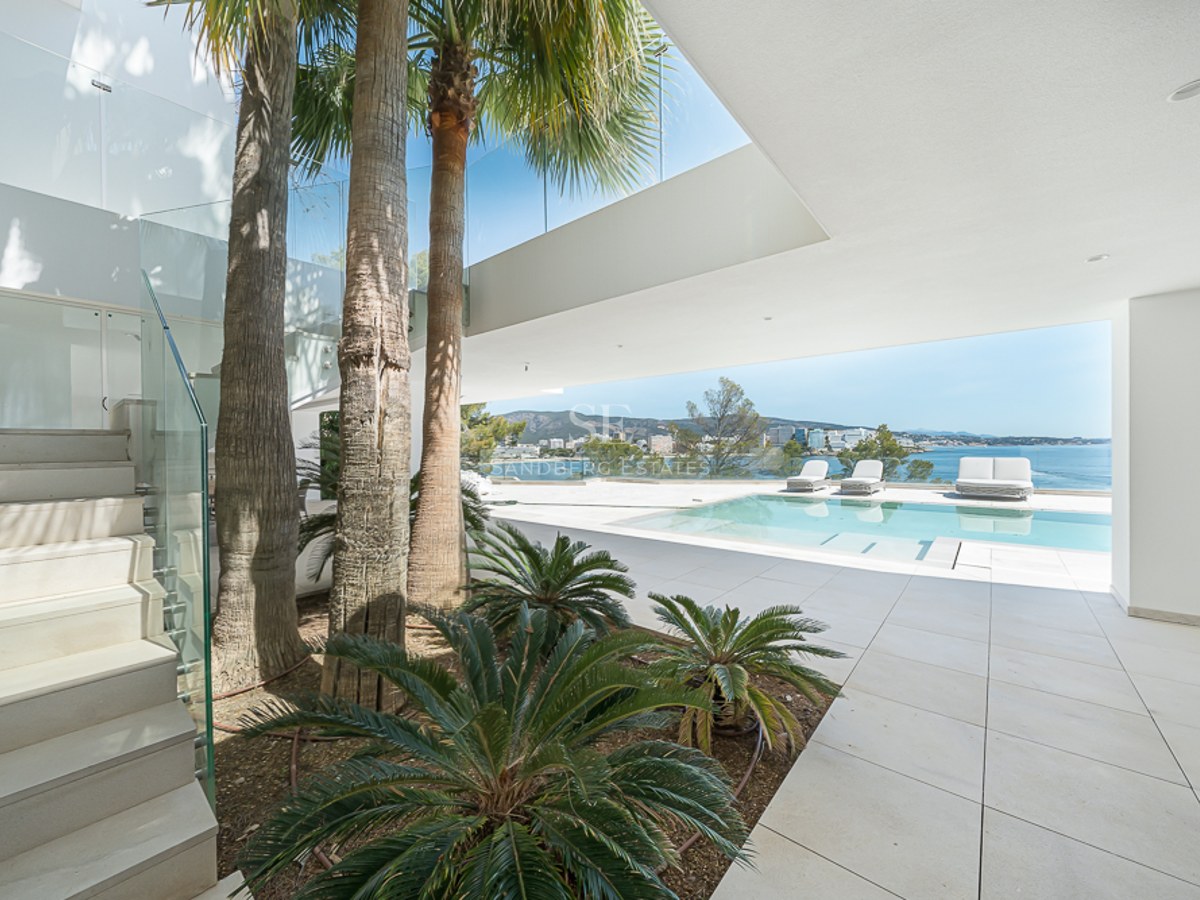 Terraza de villa moderna con piscina, palmeras y barandillas de cristal con vistas al mar Mediterráneo azul.