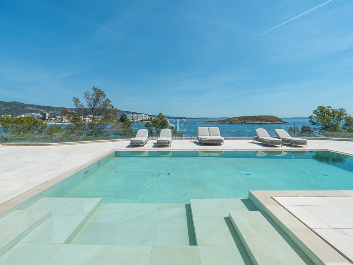 Una piscina turquesa en una terraza de piedra con tumbonas con vistas al mar Mediterráneo y una isla lejana.