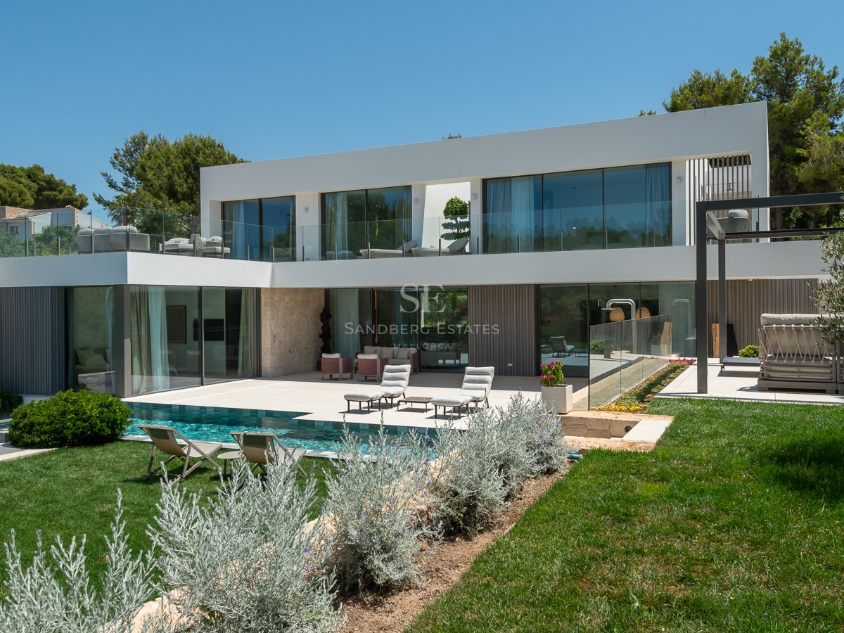Façade arrière d'une villa moderne blanche avec piscine turquoise, pelouse, accents en pierre et balcons en verre.