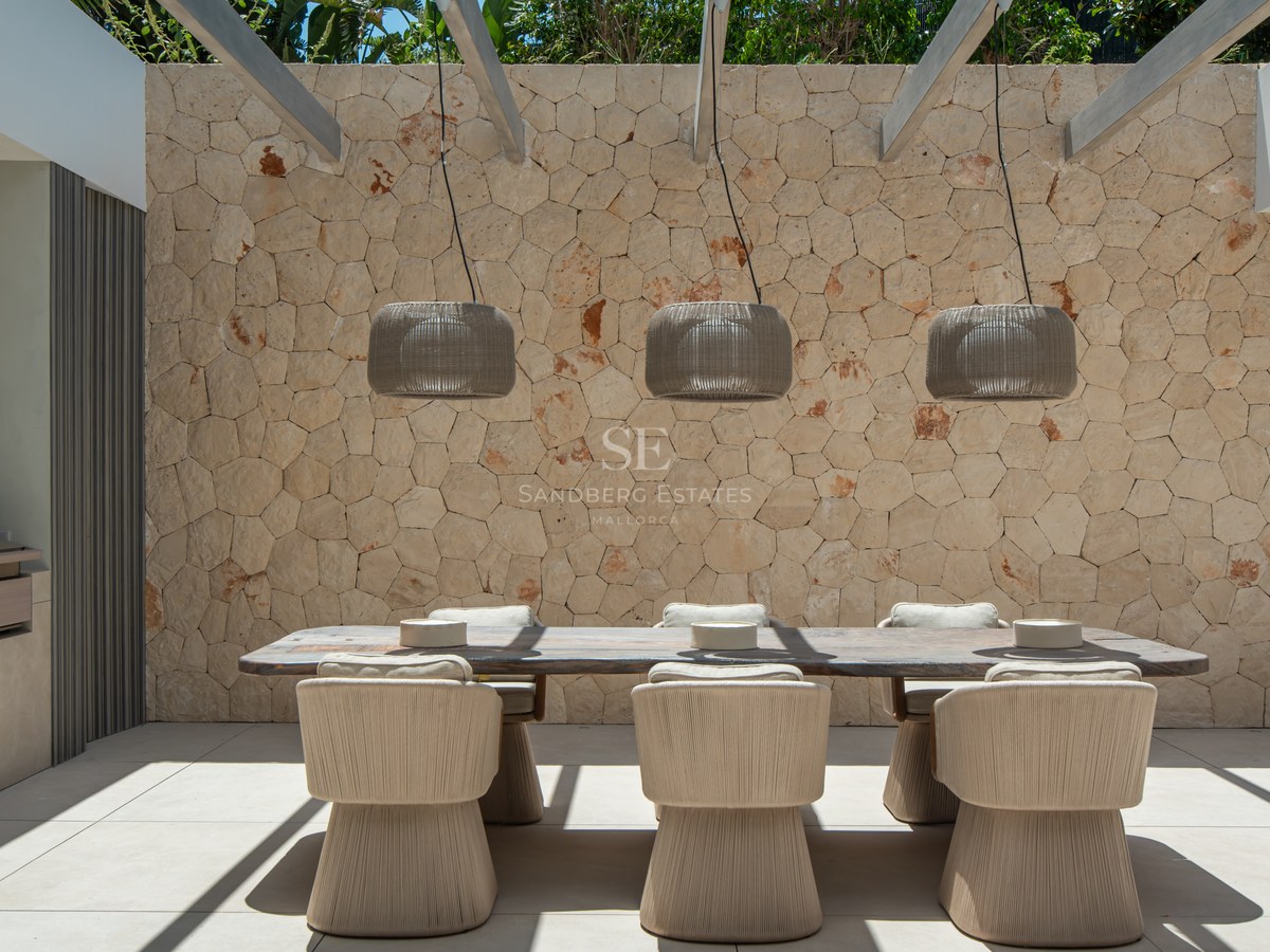 Espace repas extérieur chic avec table en bois, chaises en corde et pergola devant un mur en pierres apparentes.