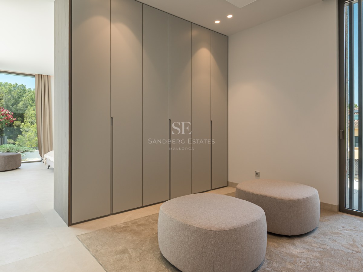 Dressing minimaliste avec armoires du sol au plafond, deux poufs en tissu et grandes fenêtres avec persiennes.