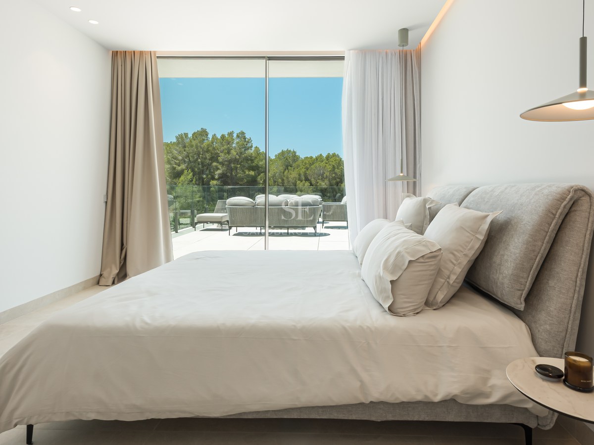 Chambre contemporaine avec grandes baies vitrées ouvrant sur une terrasse avec mobilier et vue sur les arbres.