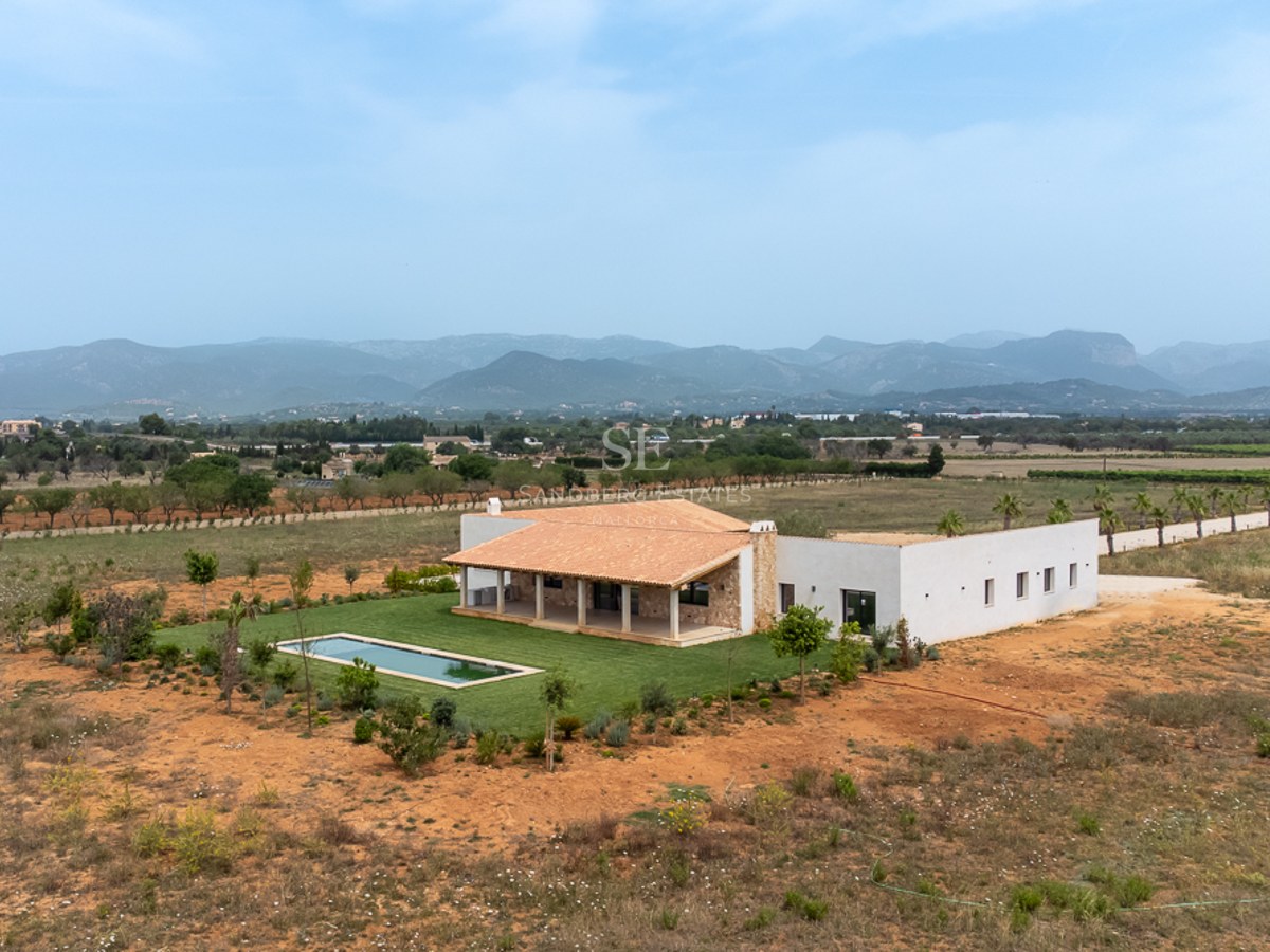 Luftaufnahme einer weißen Villa mit Pool, Terrakottadach und großem Grundstück vor Bergkulisse.