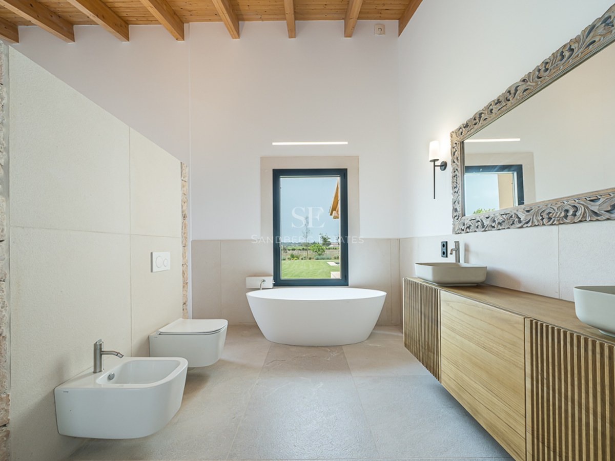 Luxuriöses Badezimmer mit freistehender Badewanne, Holzbalkendecke, Natursteinwand und Doppelwaschtisch.