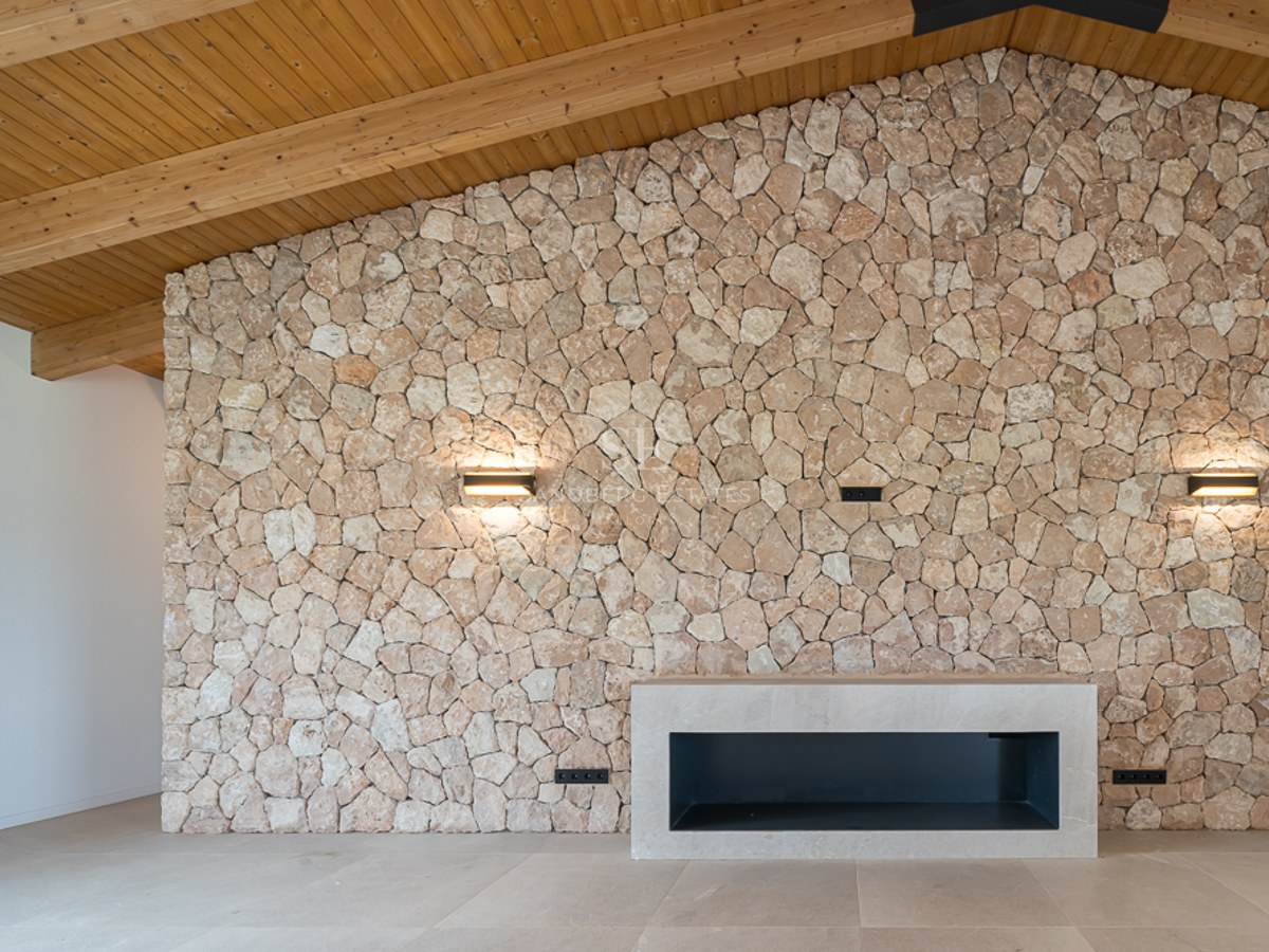 Innenansicht mit großer Natursteinwand, modernem Kamin und hoher Holzdecke mit Balken.