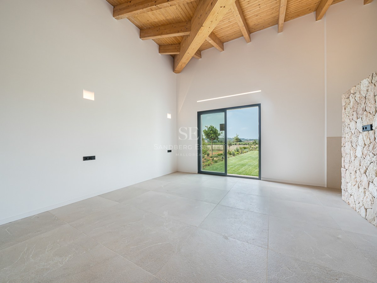 Leerer moderner Raum mit hoher Holzbalkendecke, Natursteinwand und Glastür zum grünen Garten.
