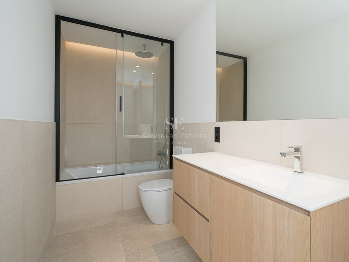 Modernes Bad mit schwebendem Eichen-Waschtisch, Steinfliesen und Badewanne mit schwarzer Glastrennwand.