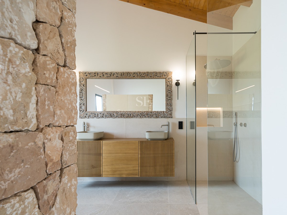 Modernes Badezimmer mit rustikaler Steinwand, Holzbalkendecke, Glasdusche und schwebendem Doppelwaschtisch.