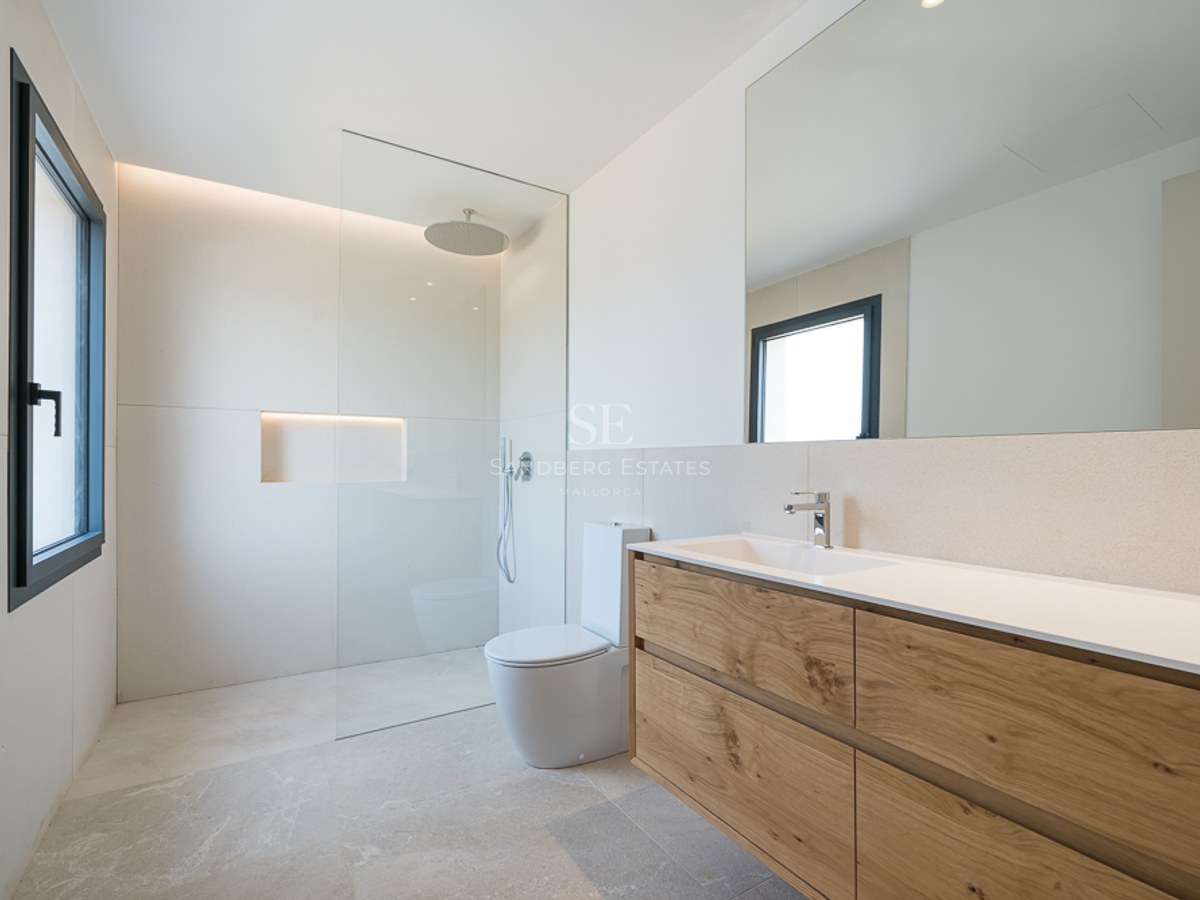 Helles Badezimmer mit Holzwaschtisch, großem Spiegel, bodengleicher Dusche und beigen Natursteinfliesen.