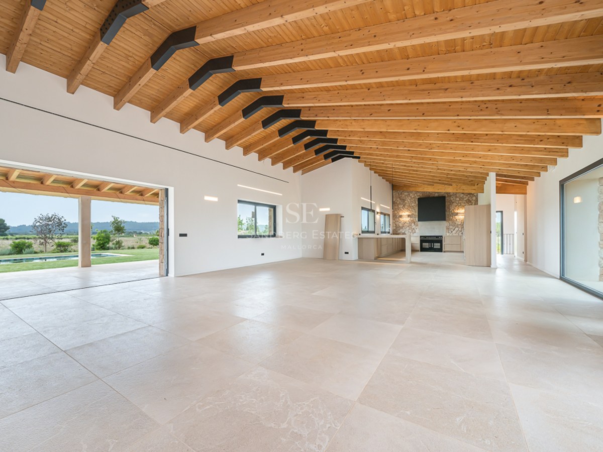 Großes modernes Wohnzimmer mit Holzbalkendecke, Steinfußboden und Glasschiebetüren zum Pool und Garten.