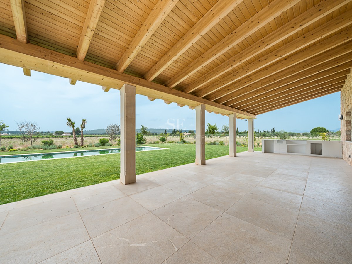 Weite überdachte Terrasse mit Natursteinboden und Holzbalkendecke mit Blick auf Garten und Pool.