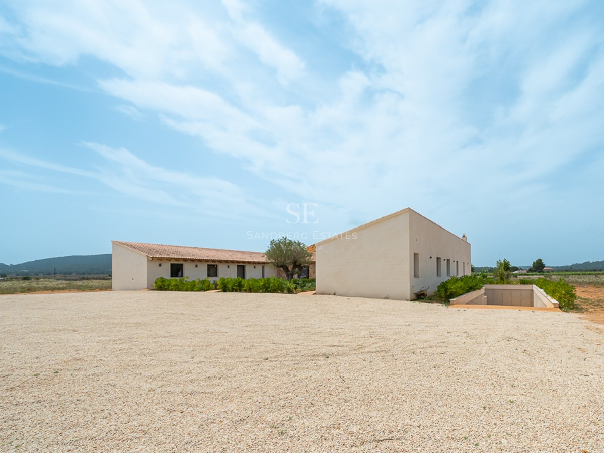 L-förmige cremefarbene minimalistische Villa mit Terrakottadach und Kiesauffahrt unter strahlend blauem Himmel.