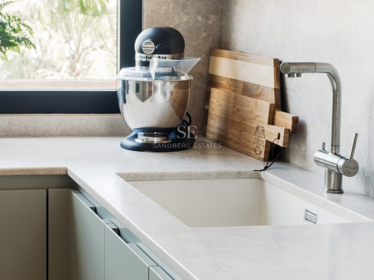 Primer plano de un fregadero de cocina con grifo de acero, encimera de piedra, batidora y tablas de madera.