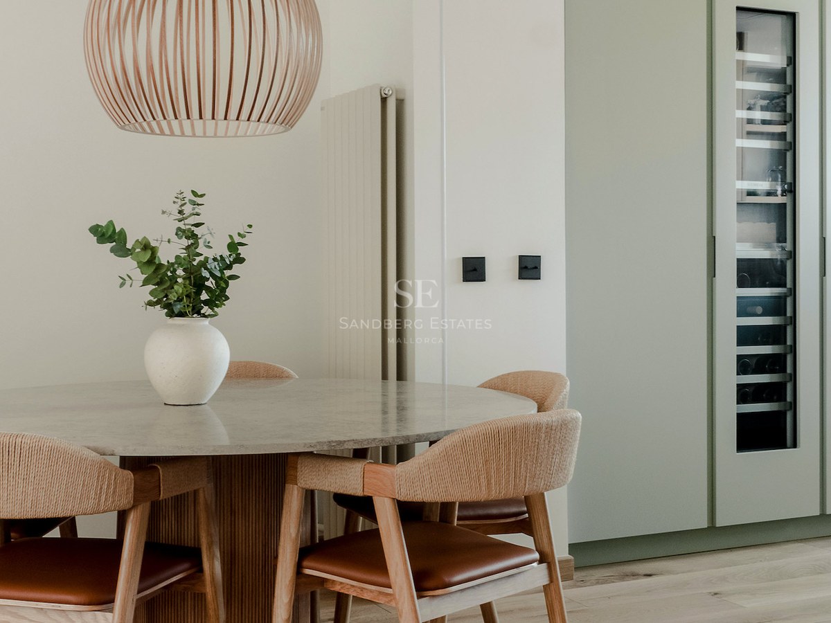 Comedor moderno con mesa de piedra, sillas de madera tejida y una vinoteca empotrada en armarios verde salvia.