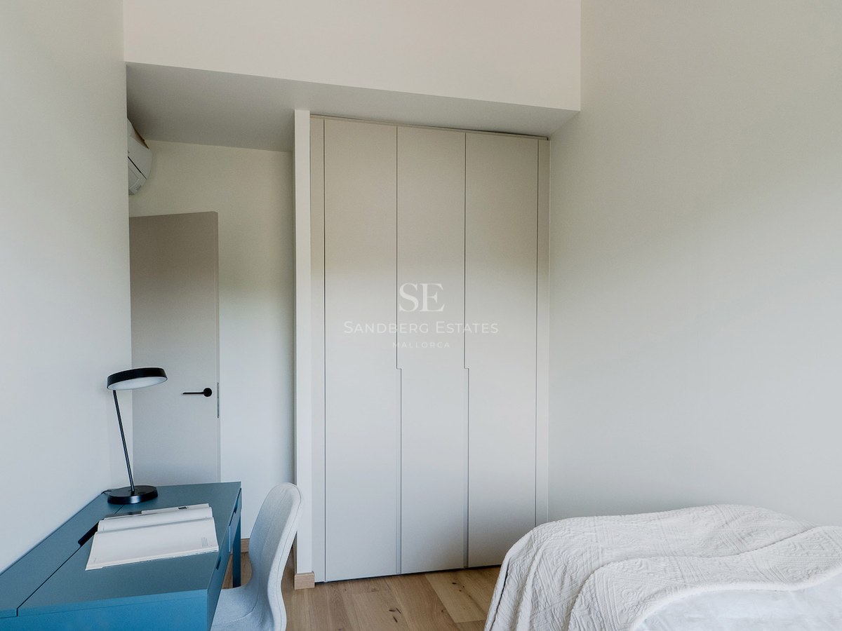 Dormitorio moderno con armario empotrado blanco, escritorio azul, lámpara negra y suelo de madera clara.