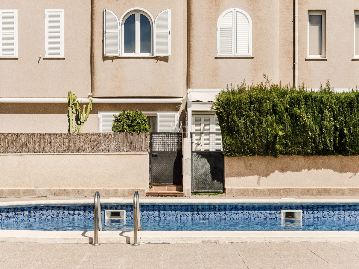 Piscina exterior con mosaicos azules frente a una fachada beige con persianas blancas.