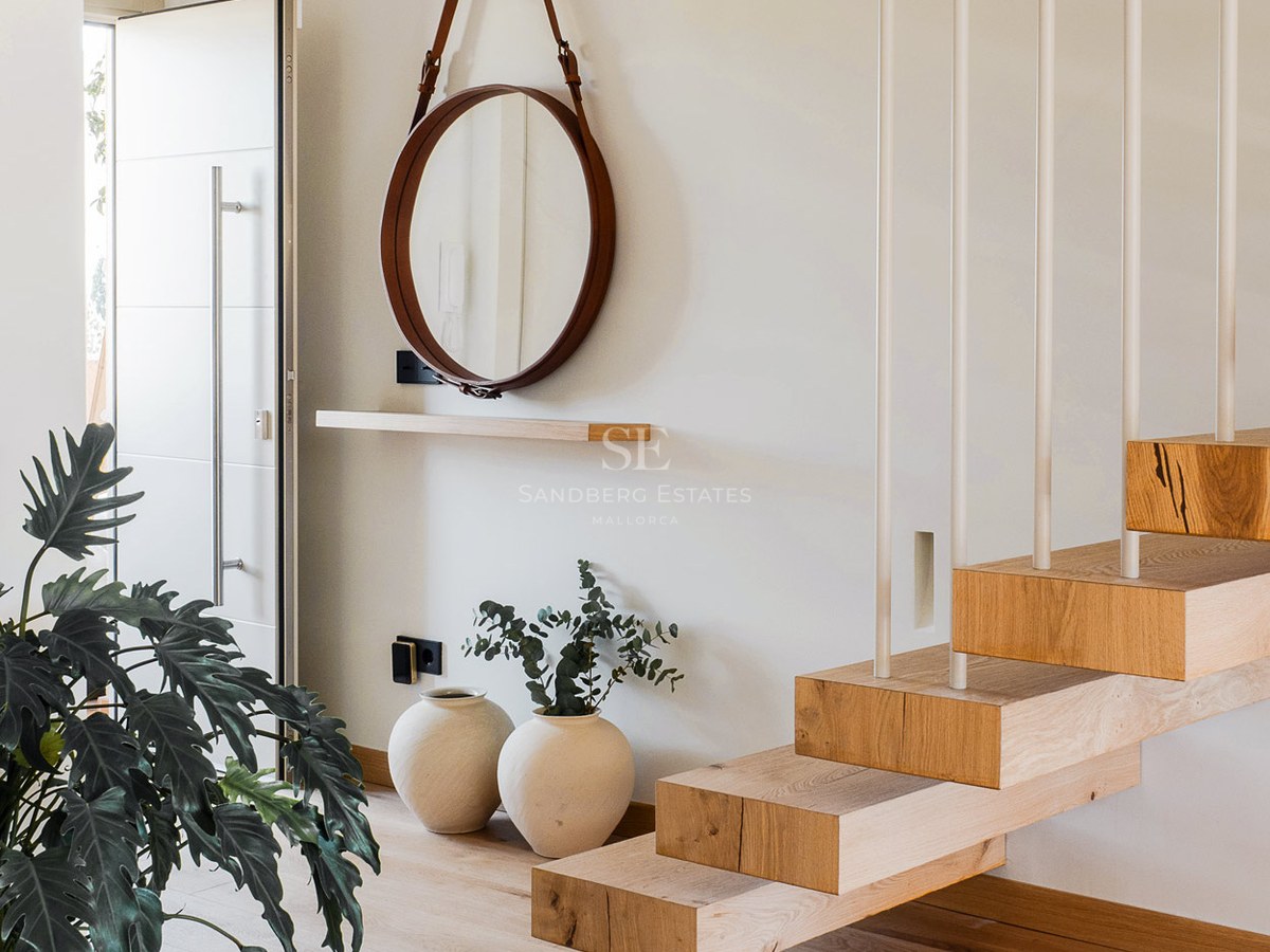 Entrada con escalones de madera flotantes, espejo circular con correa de cuero y decoración minimalista.