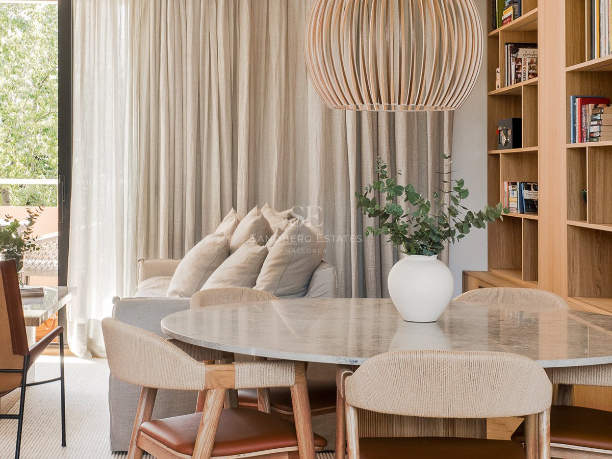 Comedor luminoso con mesa de mármol, sillas de madera y cuero, y una gran lámpara colgante de listones de madera.